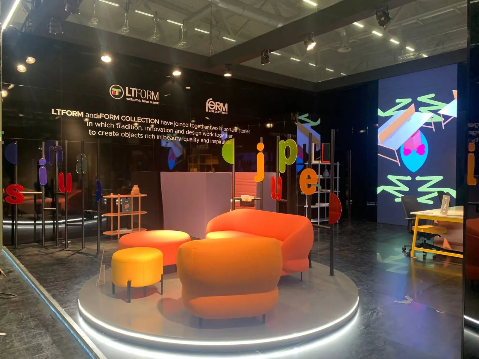 Stand LTFORM e Form Collection a Orgatec, area salotto con sedute arancioni su pedana illuminata