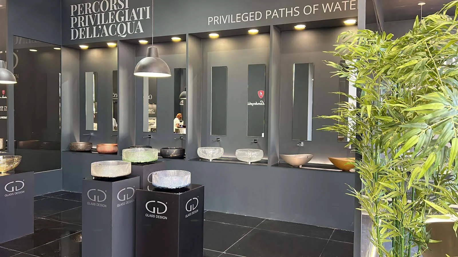 Parete espositiva dello stand Glass Design Italy a Cersaie, lavabi in vetro su piedistallo