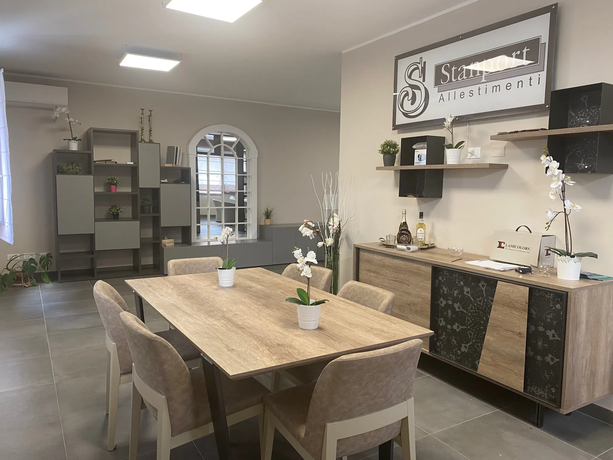 Showroom Stanport con tavolo e sedie in rovere, libreria modulare grigia e madia con insegna Stanport Allestimenti a parete